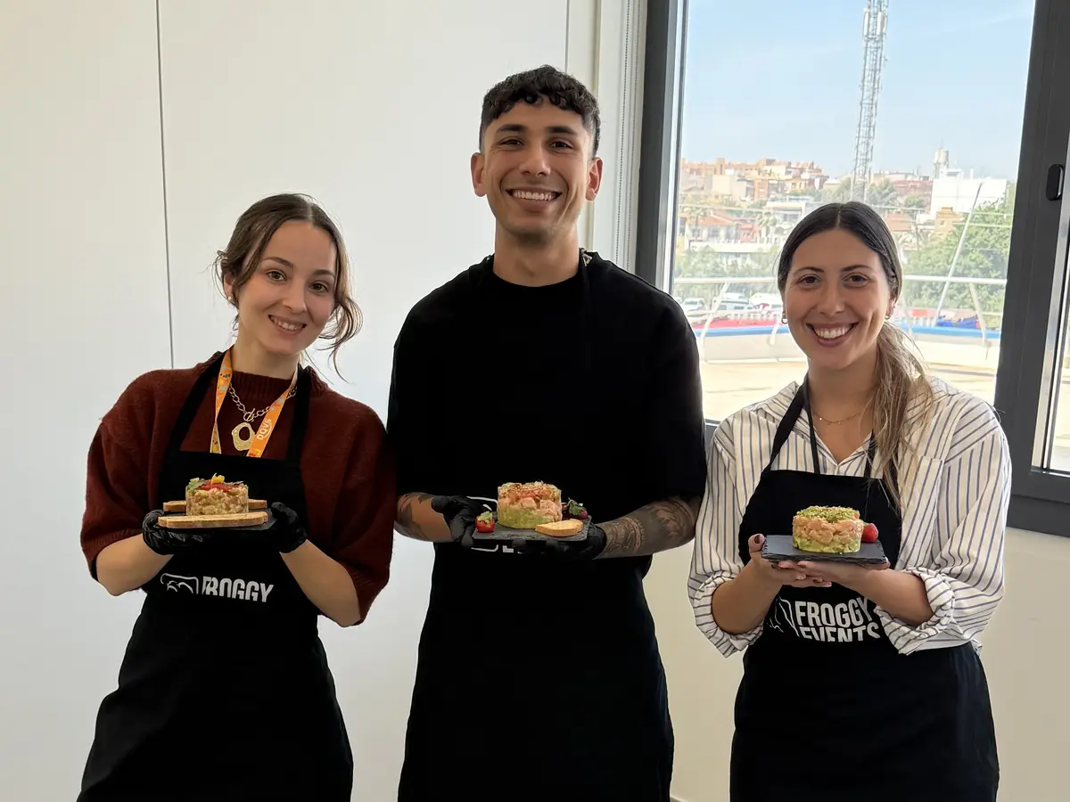 Tres participantes con delantales Froggy Events mostrando sus platos en el taller de cocina de empresa