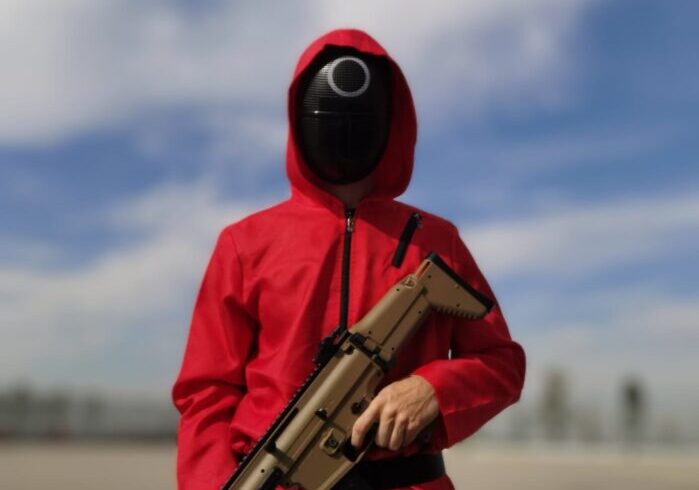 Actor disfrazado de guardia rojo con máscara y réplica de arma en la actividad temática El Juego del Calamar para empresas