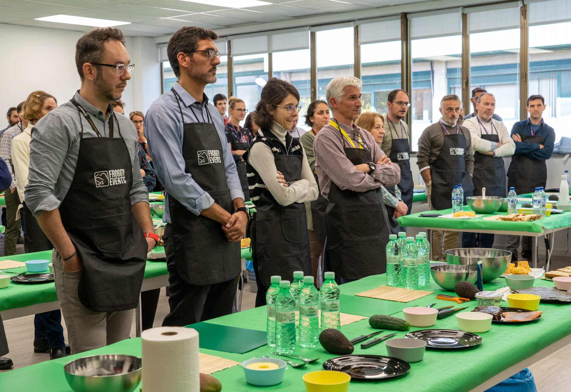 Equipo de empleados con delantales corporativos escuchando atentamente las instrucciones del chef en taller de sushi