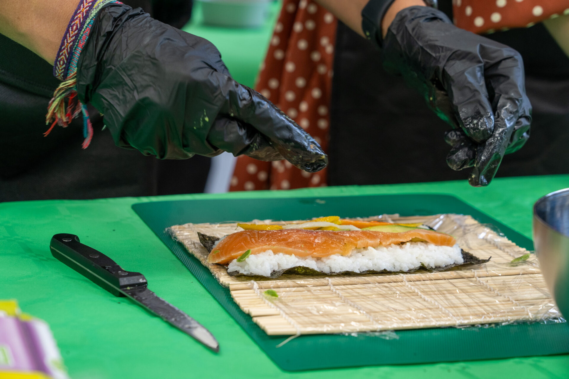 Manos con guantes negros colocando láminas de salmón fresco sobre el arroz para hacer un maki en taller de cocina