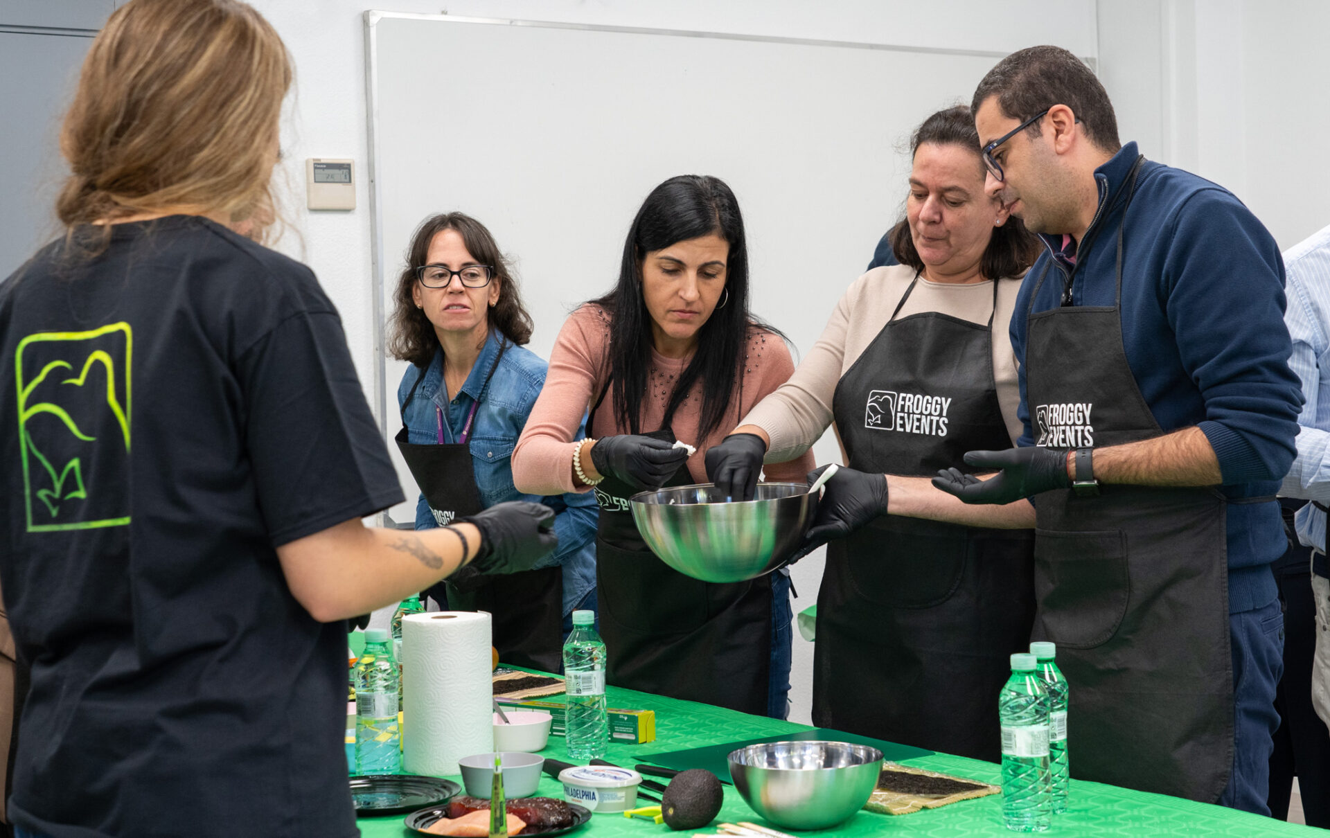 Grupo de participantes aprendiendo a mezclar y aderezar el arroz para sushi en un bol metálico bajo supervisión