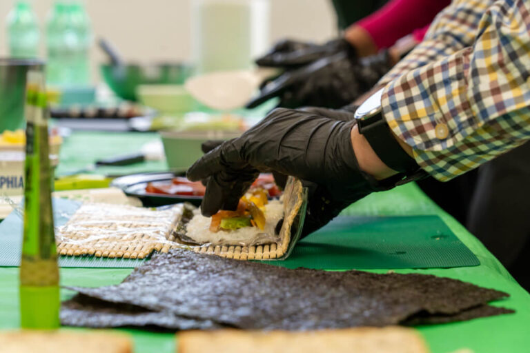 Primer plano de manos con guantes negros enrollando un maki de salmón y aguacate en actividad de team building