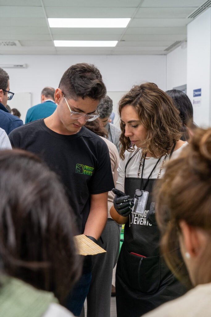 Dos compañeros de trabajo colaborando concentrados para enrollar sushi en taller de cocina para team building